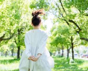緑の森をスキップする女性の後ろ姿